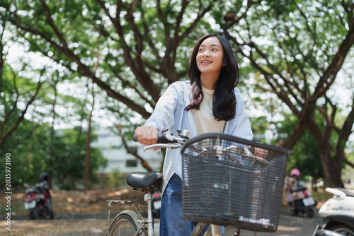 Young woman smiling walking bicycle on campus path