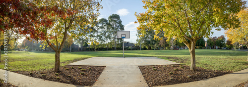Φωτογραφία Panoramic view of an outdoor half basketball court framed by autumn trees in spacious municipal suburban park