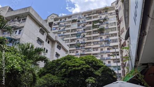 Old apartment building in Ho Chi Minh City, Vietnam: Retro residential complex with dense balconies and windows towering behind lush trees