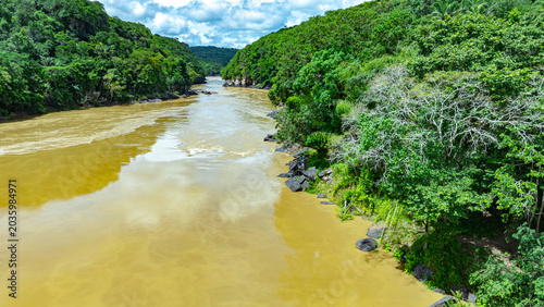 Konstfotografi The murky waters of Raudal del Guayabero reflect lush green vegetation along the banks under a partly cloudy sky