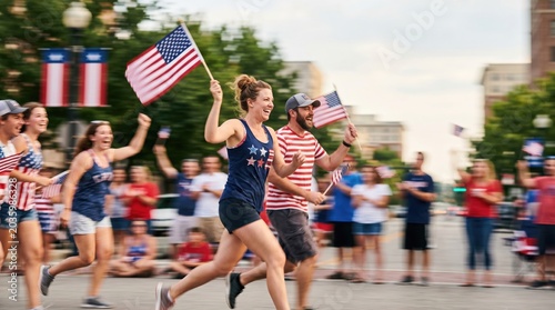 Group of Young Adult Men and Women Running in Patriotic Fun Run Parade Holding American Flags Celebrating Independence Day Outdoors in Summer