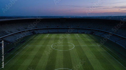 High-angle drone perspective of a serene, unpopulated soccer stadium center circle during twilight. Offers massive copy space for sports broadcasting intros or corporate event announcements.