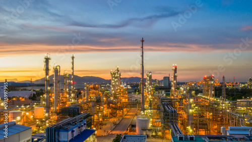 Foto Industrial Complex at Dusk: An expansive industrial facility, illuminated by the warm glow of countless lights, stretches across the landscape as the sun dips below the horizon
