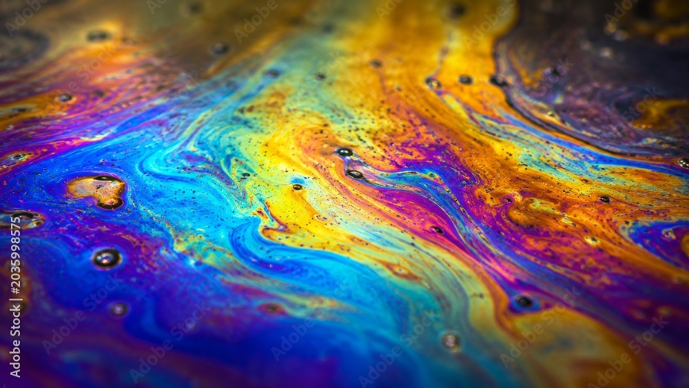 Fototapeta premium A vibrant, swirling pattern of colors resembling oil on water, showcasing hues of blue, purple, yellow, and orange against a dark background.