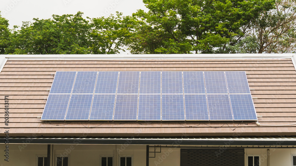 Fototapeta premium Solar panels installed on the roof of a house with green trees in the background. Concept of renewable energy, eco-friendly living, and alternative sustainable power for modern homes.