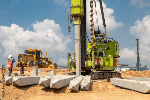 Photos Foundation Building: Heavy construction machinery, including a pile driver and grader, works on-site to lay the groundwork for a new structure, under a clear blue sky