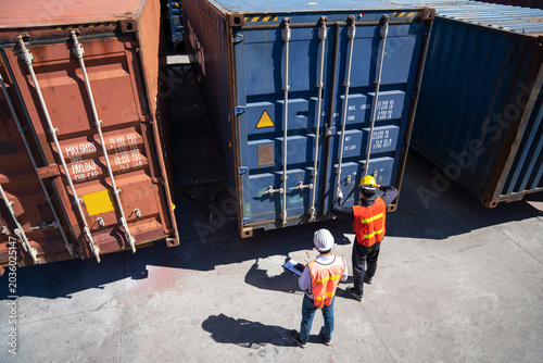 Φωτογραφία Shipping Containers at Port: Two workers in high-visibility vests oversee the loading and unloading of large shipping containers at a busy port, symbolizing global trade and logistics