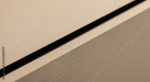 Thin dark velvet ribbon detail applied with extreme precision on a textured beige surface