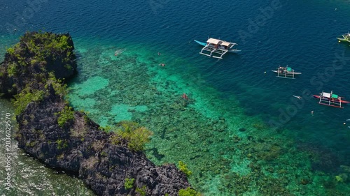 Drone forward tracking shot tilting down over a traditional outrigger boat on a clear coral reef flat in Coron, Palawan.