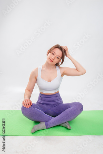 Full length portrait of young athletic woman sitting in lotus position on yoga mat isolated on white background.