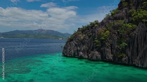 Drone orbit shot around a dramatic limestone headland cliff surrounded by turquoise ocean in Coron, Philippines.