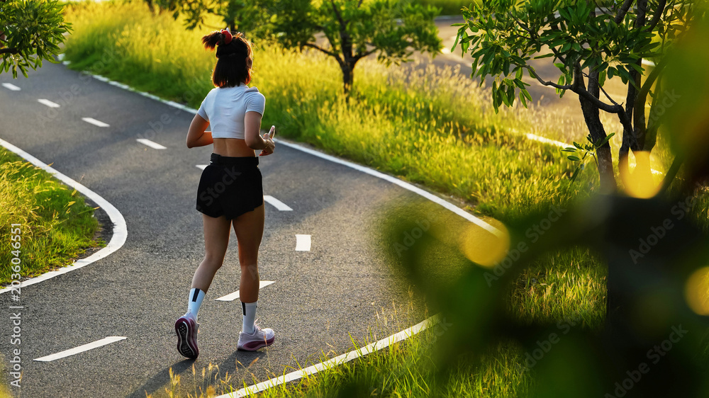 Naklejka premium Active young woman jogging on a scenic park path during beautiful golden hour sunset for health and fitness concept