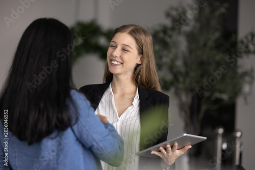 Foto Two young businesswomen, workmates greeting each other in workplace with handshake gesture, express friendly relations, mutual respect
