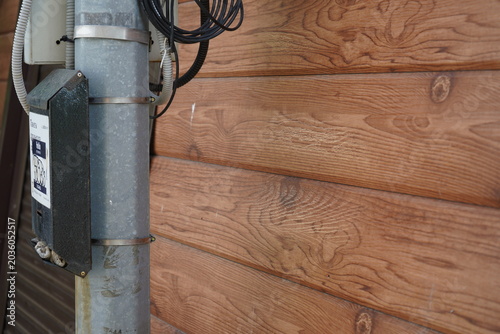 Close-Up of a Utility Pole Equipped with Electrical Components Next to a Wooden Wall Featuring Distinct Grain Patterns and Natural Textures