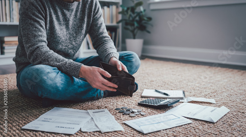 Man holding an empty wallet while managing household bills, receipts, coins, and calculator at home, showing financial stress, debt, budgeting, poverty, and cost of living crisis.