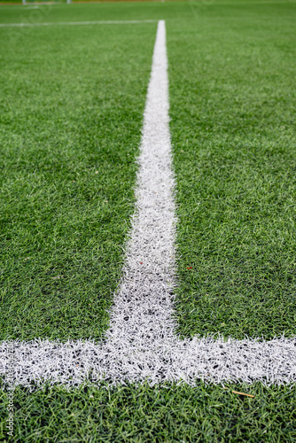 Close up view of white field marking line on green artificial grass football pitch. Sports background with texture and perspective.