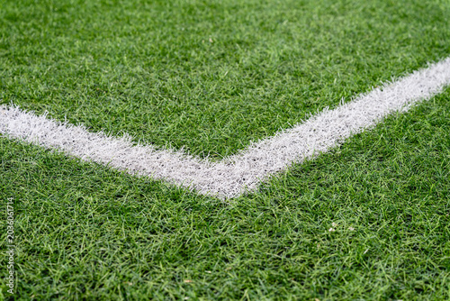 Close up view of white corner marking on green artificial grass football field. Sports background with texture and copy space.