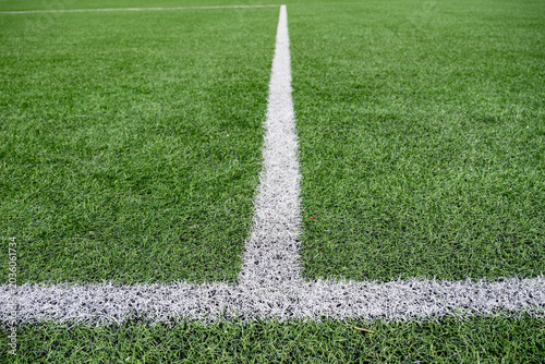 Close up view of white field marking line on green artificial grass football pitch. Sports background with texture and perspective.