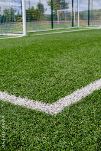 Corner marking of football field with goal net in background on green artificial grass. Sports venue and competition concept.