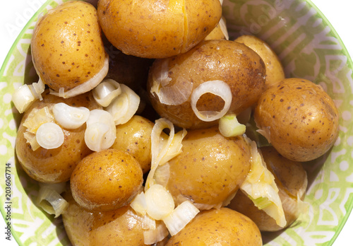 Salad potatoes mixed with spring onions and butter in a green patterned bowl on a white wood background.