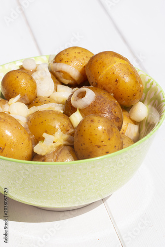 Salad potatoes mixed with spring onions and butter in a green patterned bowl on a white wood background.
