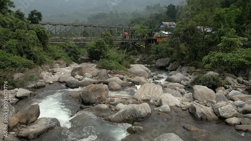 A cinematic drone shot of a rocky mountain river flowing under a vintage iron bridge in Sittong, North Bengal, India. nature scene for travel.