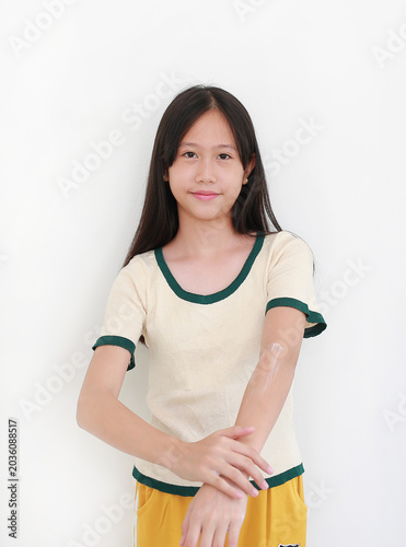 Portrait of smiling young Asian girl applying moisturizing skin cream onto her arm, isolated on a white background.