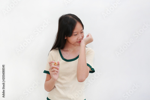 Beautiful Asian teenage girl holding a perfume bottle and smelling the pleasant scent on her wrist, standing isolated on white background.