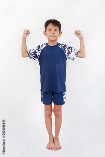 Full-length shot of young Asian boy in blue and camouflage swimwear standing against white background, confidently showing his strong arm muscles.