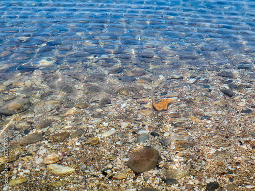 Clear Shallow Water Over Pebble Beach With Gentle Ripples And Sunlit Stones At Shoreline