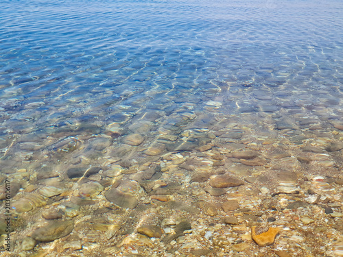 Clear Shallow Water Over Pebble Beach With Gentle Ripples And Sunlit Stones At Shoreline