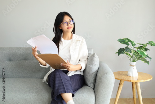 Tableau sur toile A young woman at home sits on the sofa, anxiously flipping through bills and documents looking for important documents among the financial statements, a thoughtful expression staring upwards