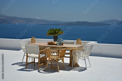 Fotografie Landscape with scenic view of a dining table and chairs on a whitewashed terrace overlooking the caldera in Santorini island, Cyclades Greece