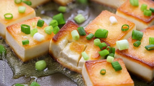 Panfried Tofu Pieces Garnished With Chopped Scallions And Drizzled Sesame Oil Shine In Rustic Kitchen Setting