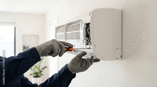 Technician repairing air conditioner with screwdriver. Man fixing home climate control system. Professional HVAC maintenance and installation service. Equipment service and repair concept.