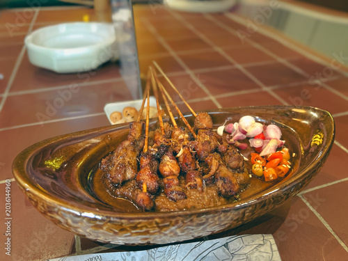 Several skewers of satay served with traditional peanut sauce and seasonings on an elegant plate at an Indonesian restaurant.