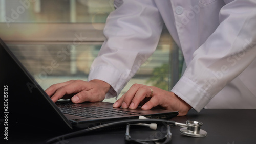 Focused doctor performs clinical data integration on medical laptop next to stethoscope for patient health record management