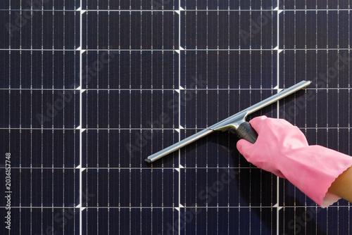 Foto Woman hand in pink rubber protective glove holding squeegee with rubber blade and cleaning dark black solar panels