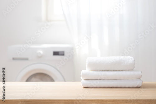 Foto Stack of white clean textile on table with blurred laundry room interior backgro