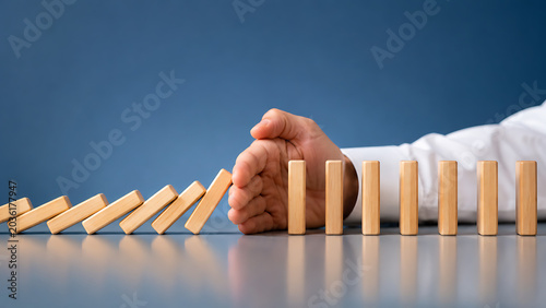 Hand stopping falling wooden domino blocks symbolizing business risk prevention crisis management and problem solving protection strategy