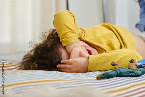 Fotografie Upset toddler crying on bed covering face. unrecognizable person