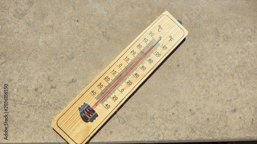  a wooden thermometer lying on bright concrete under direct sunlight representing extreme summer heat anomaly dangerously high temperatures global warming and ecological threat to people