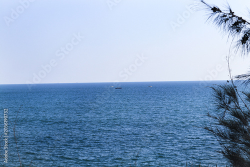 Distant Fishing Boats on a Calm Blue Ocean Horizon. Wide Angle View of Deep Blue Sea with Small Vessels. Clear Blue Sky Over Vast Open Water Surface. Tranquility and Solitude in the Open Ocean.