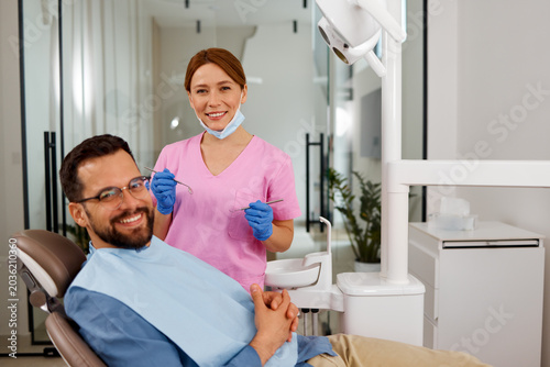 Quadro su tela Dentist holding instruments with a male patient sitting in a dental chair smilin