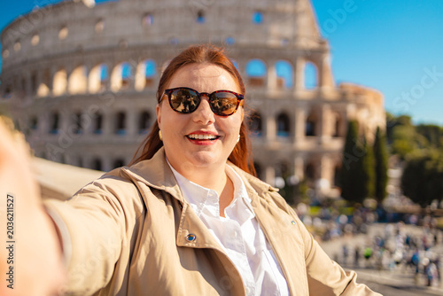 Happy young woman taking a selfie in front of the colosseum while in Rome, Italy. High quality photo