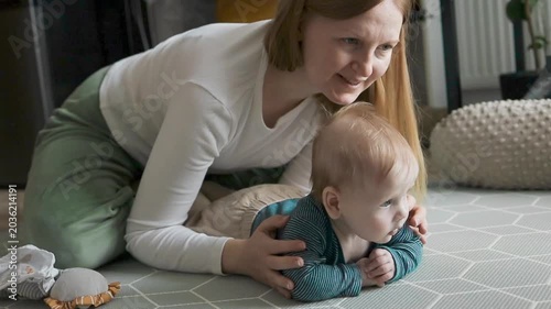 Smiling mom bonding and playing with little son on the floor at home.