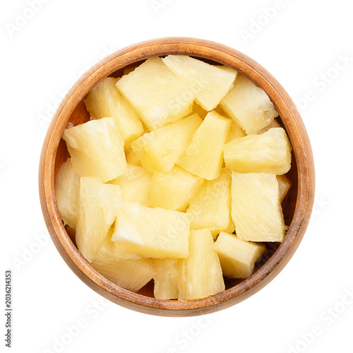 Canned pineapple chunks, in a wooden bowl. Ripe pineapples, cut into block shaped pieces, boiled in its own juice, and then tinned. Isolated, close-up, from above, on white background, food photo.