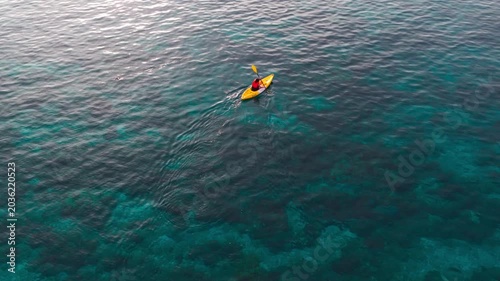 Aerial view of a woman relaxing on a yellow kayak over a beautiful coral reef in crystal clear turquoise sea water background