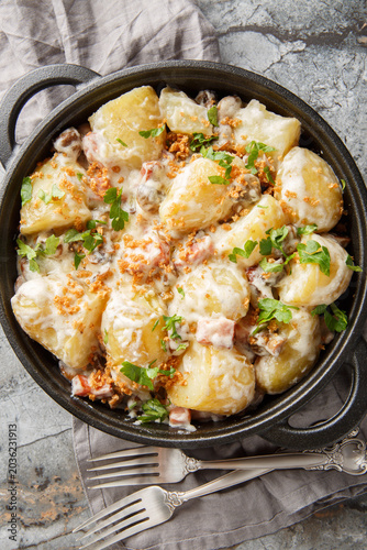 Boiled new potatoes with creamy mushroom sauce and bacon close-up in a frying pan on the table. Vertical top view from above