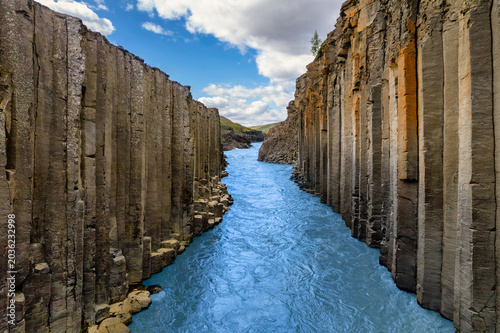 Studlagil Canyon of magnificent basalt columns, high cliff with bright turquoise glacier river, in North East Iceland, aerial shot. Famous tourist landscape